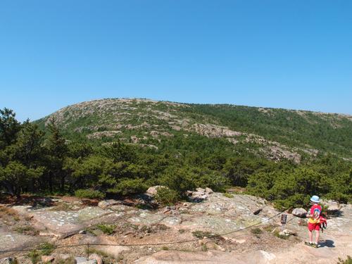 young hiker on top of Dorr Mountain looking up toward Cadillac Mountain at Acadia National Park in Maine