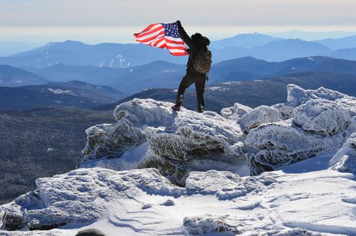 winter hiker and flag on the summit of Mount Monroe in New Hampshire