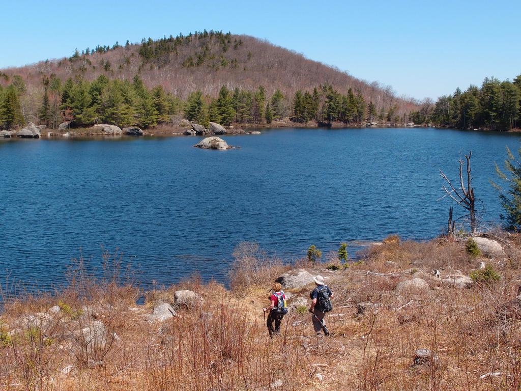 hikers at Trout Pond on the Trout-n-Bacon Trail in southwestern New Hampshire with Nancy Mountain rising on the far shore