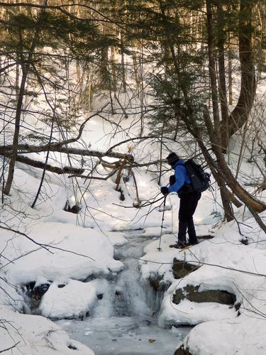 bushwhacker crossing a brook on the way to Mount Whittier in New Hampshire